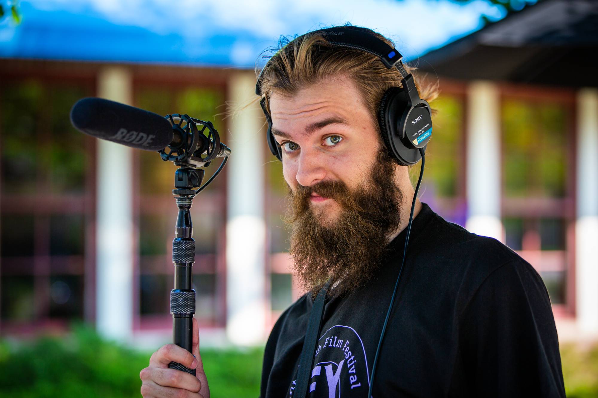 A student looks at the camera while wearing headphones and holding a boom mic